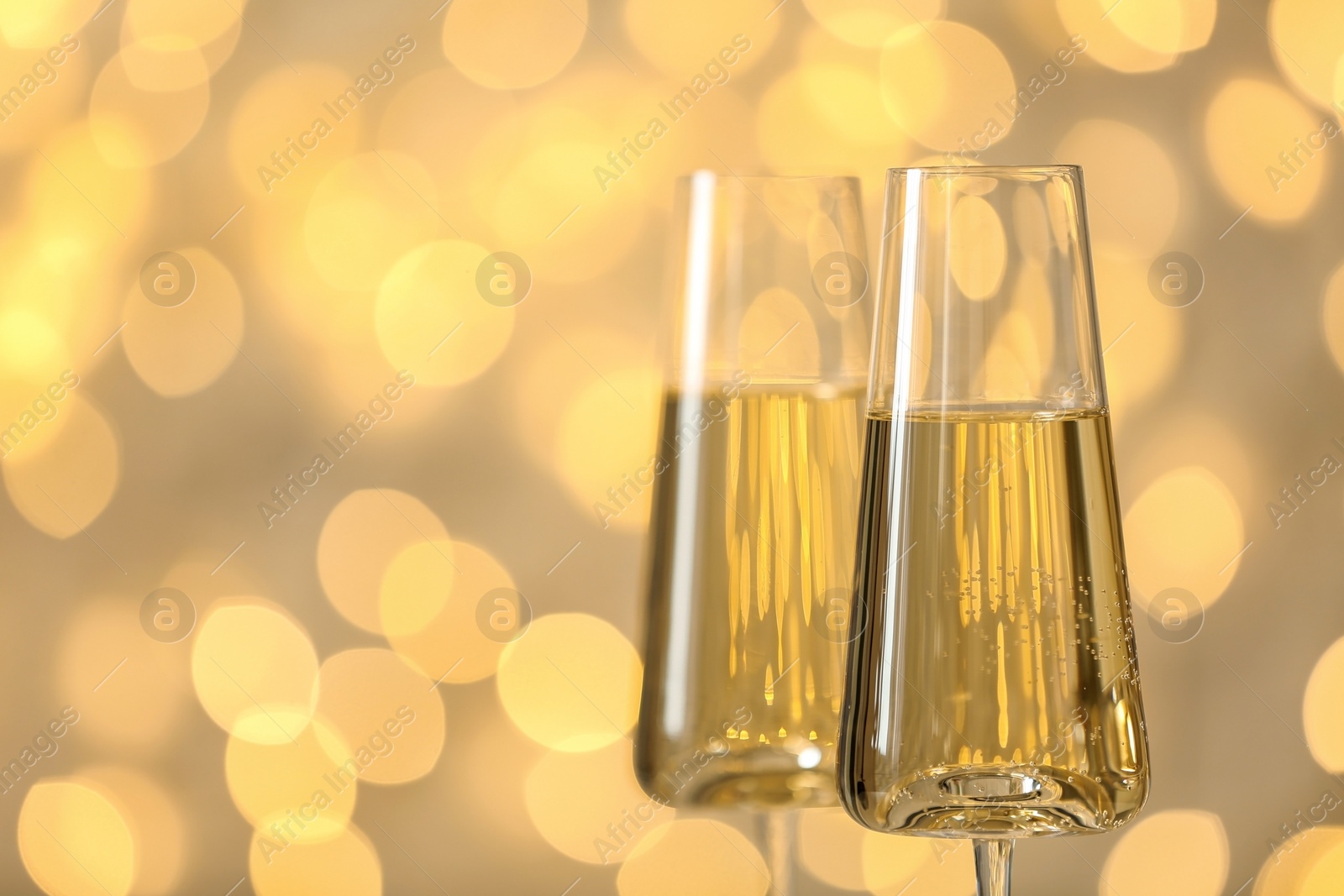 Photo of Glasses of fizzy champagne against blurred fairy lights, space for text