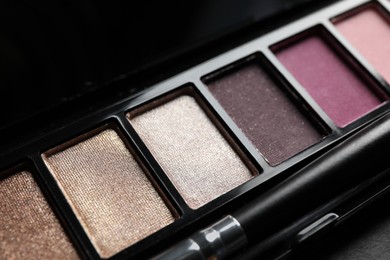 Photo of Beautiful eye shadow palette with brush on dark grey table, closeup