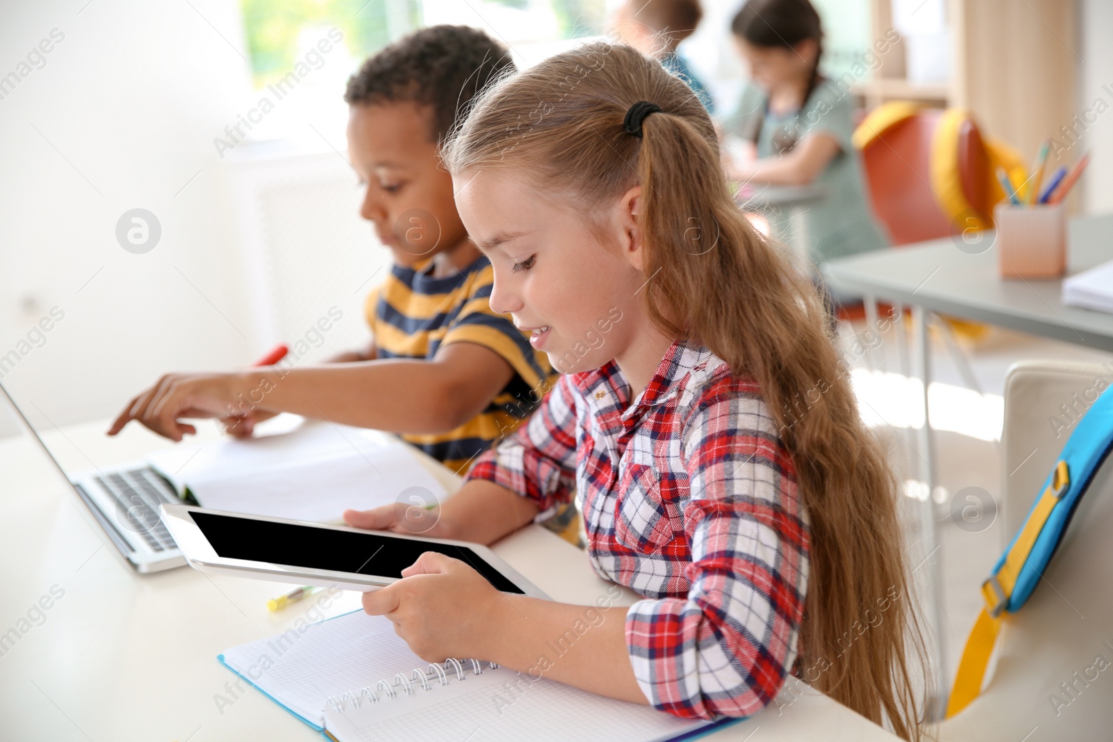 Photo of Cute little children with gadgets sitting at desk in classroom. Elementary school