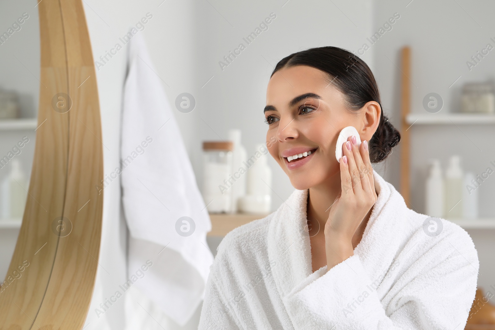 Photo of Beautiful woman removing makeup with cotton pad near mirror in bathroom, space for text