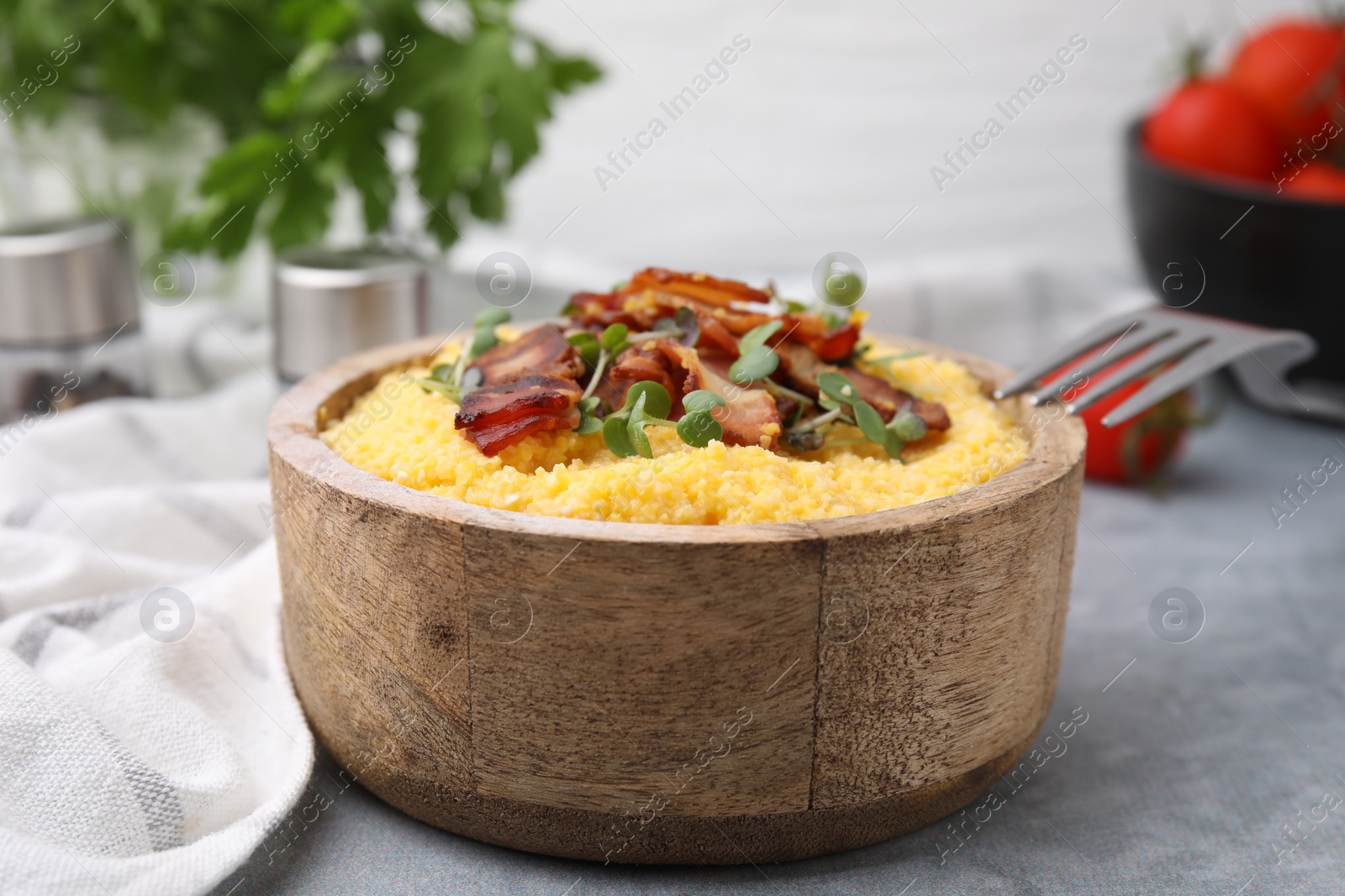 Photo of Cooked cornmeal with bacon and microgreens in bowl on light grey table, closeup