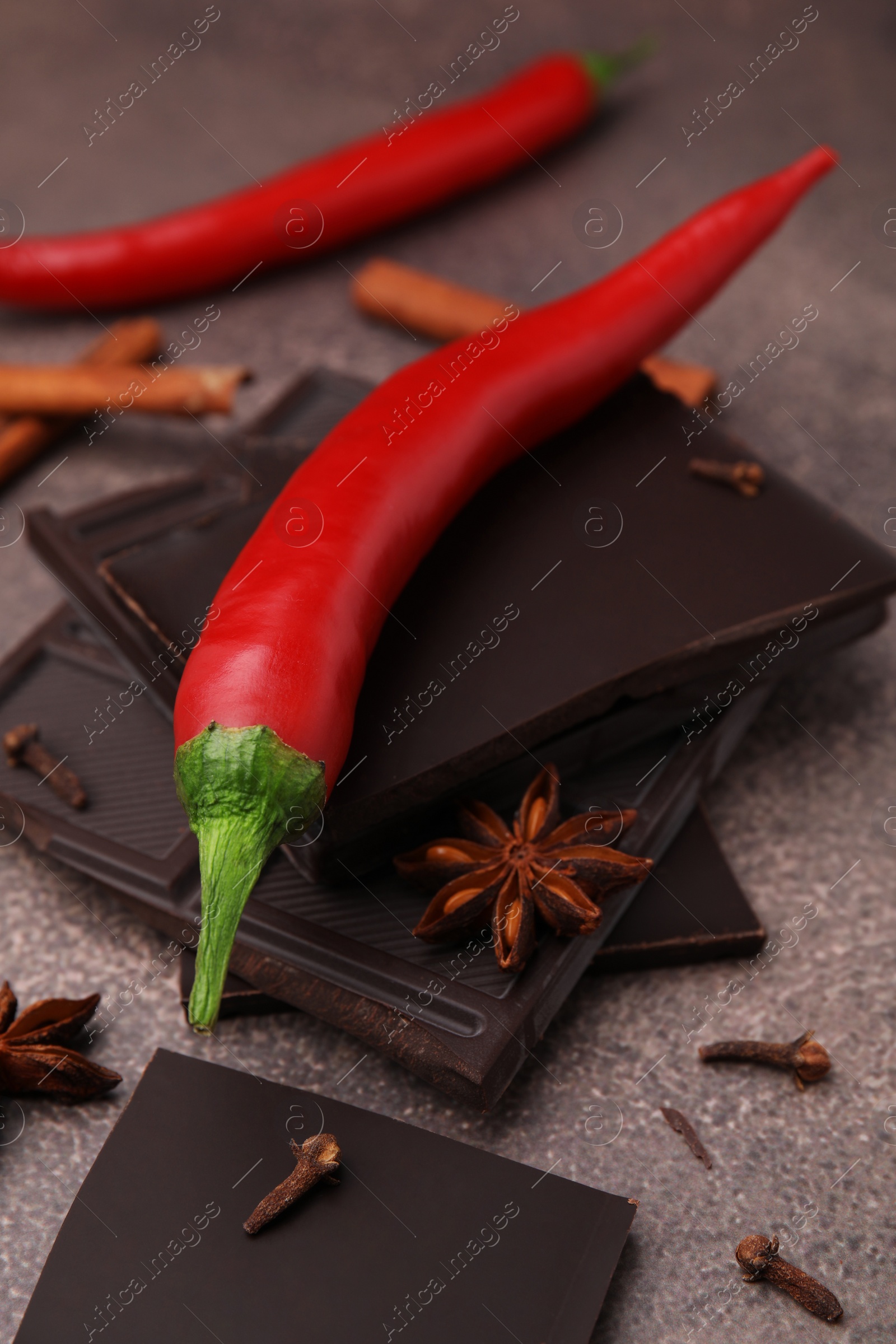 Photo of Delicious chocolate, fresh red chili pepper and spices on grey textured table, closeup