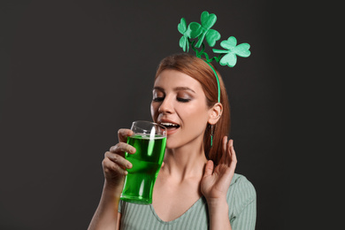 Photo of Young woman with clover headband and green beer on grey background. St. Patrick's Day celebration
