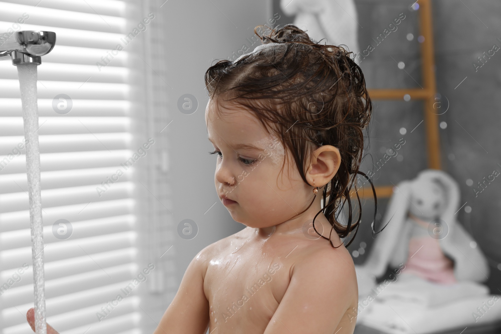 Photo of Cute little girl washing hair with shampoo in bathroom