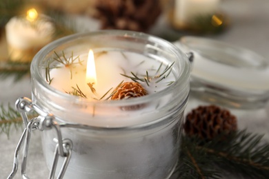 Photo of Burning scented conifer candle in glass jar, closeup view