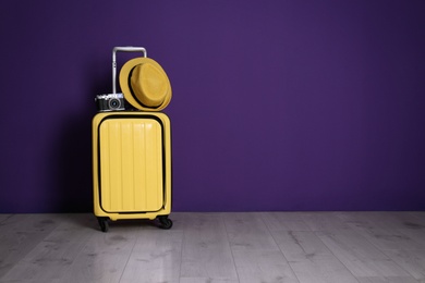 Travel suitcase with hat and camera on wooden floor near purple wall, space for text. Summer vacation