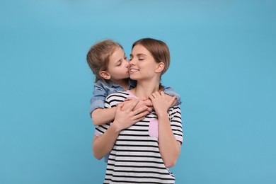 Photo of Little daughter kissing her mom on light blue background. Happy Mother's Day