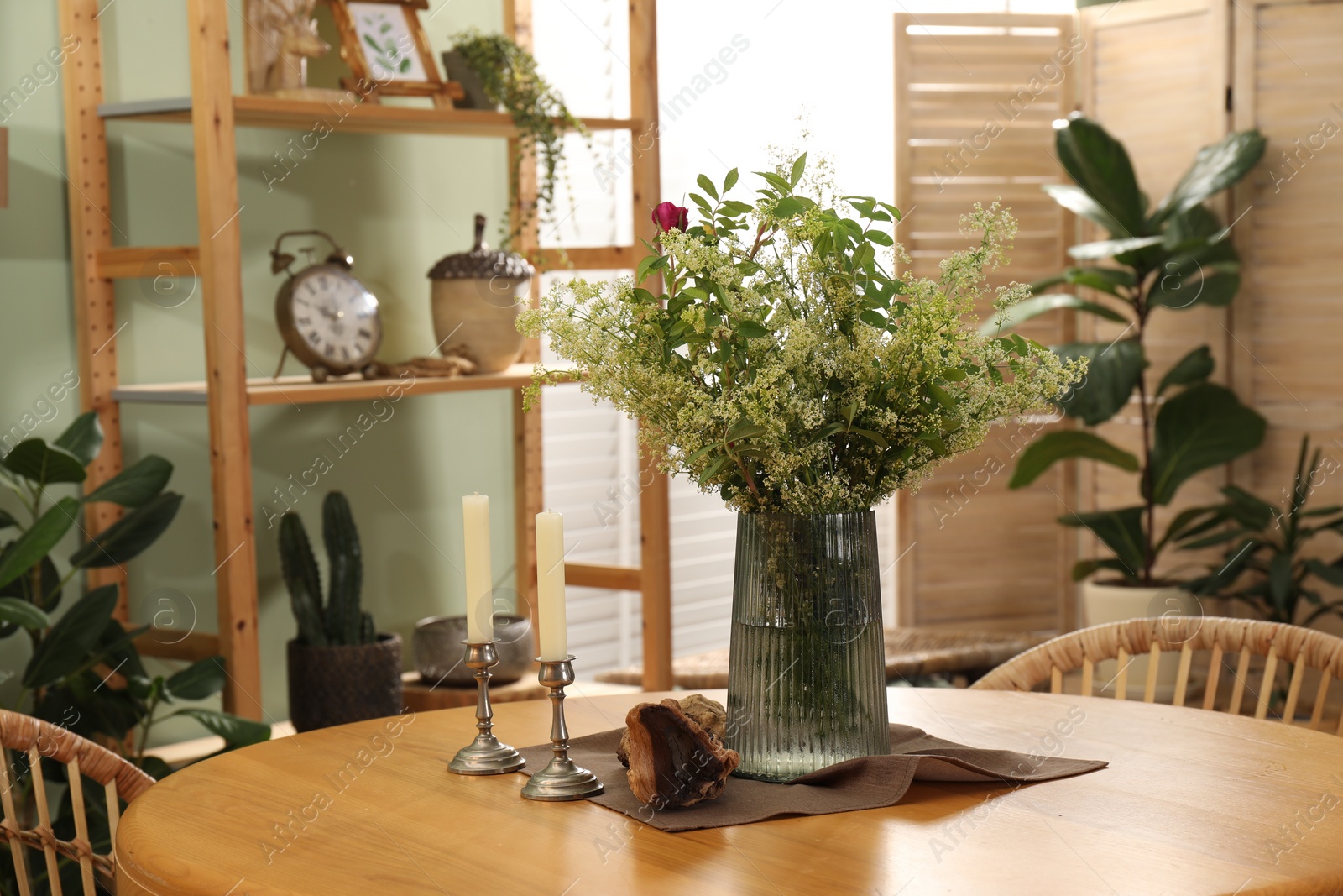 Photo of Vase with beautiful flowers and candles on wooden table in stylish dining room