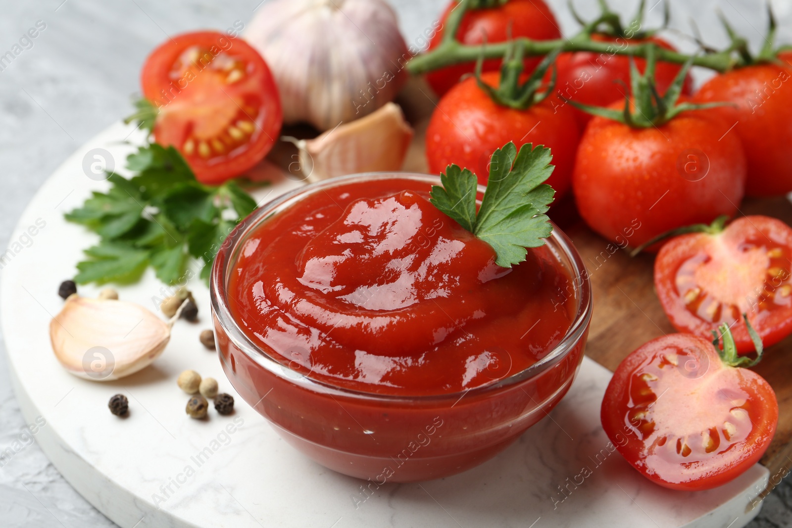 Photo of Delicious ketchup in bowl, parsley and tomatoes on grey table, closeup