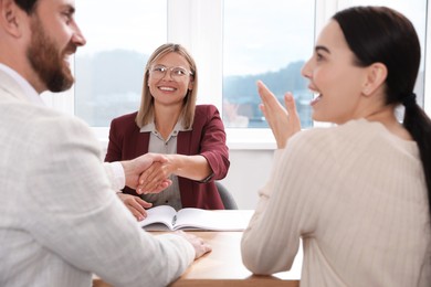 Photo of Real estate agent shaking hands with client at table in new apartment