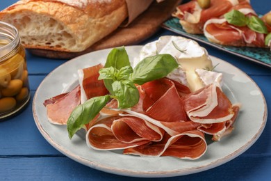 Slices of tasty cured ham, basil and cheese on blue wooden table, closeup