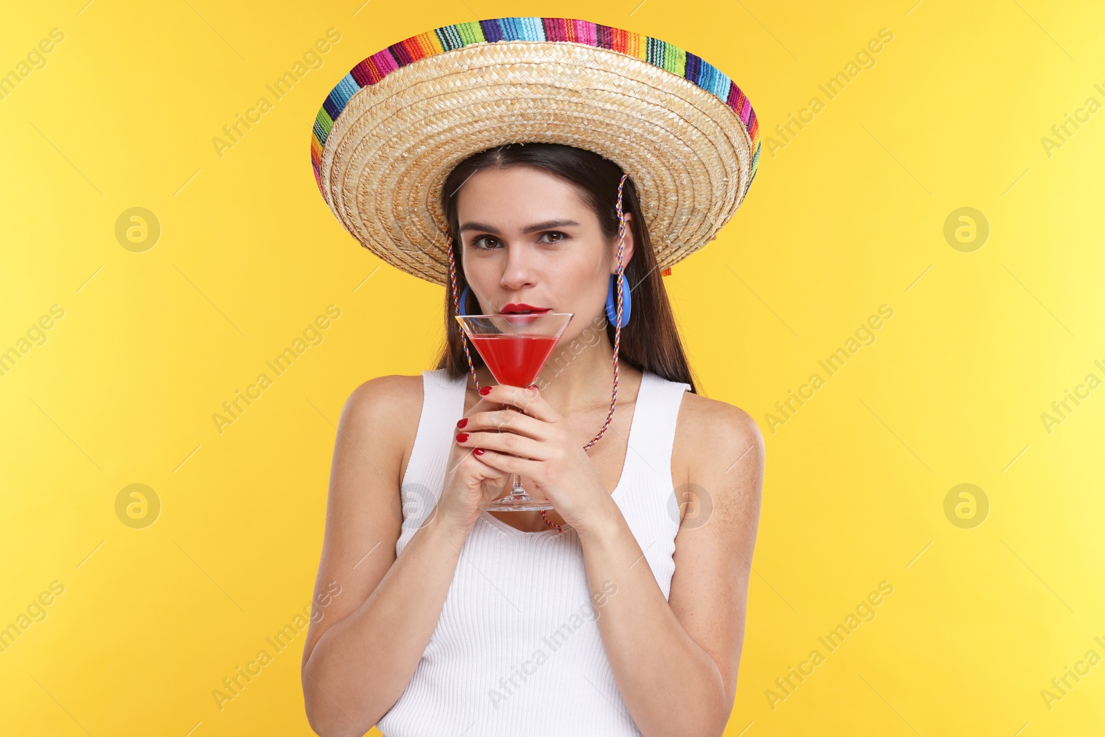 Photo of Young woman in Mexican sombrero hat with cocktail on yellow background