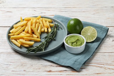 Plate with delicious french fries, avocado dip, lime and rosemary served on white wooden table
