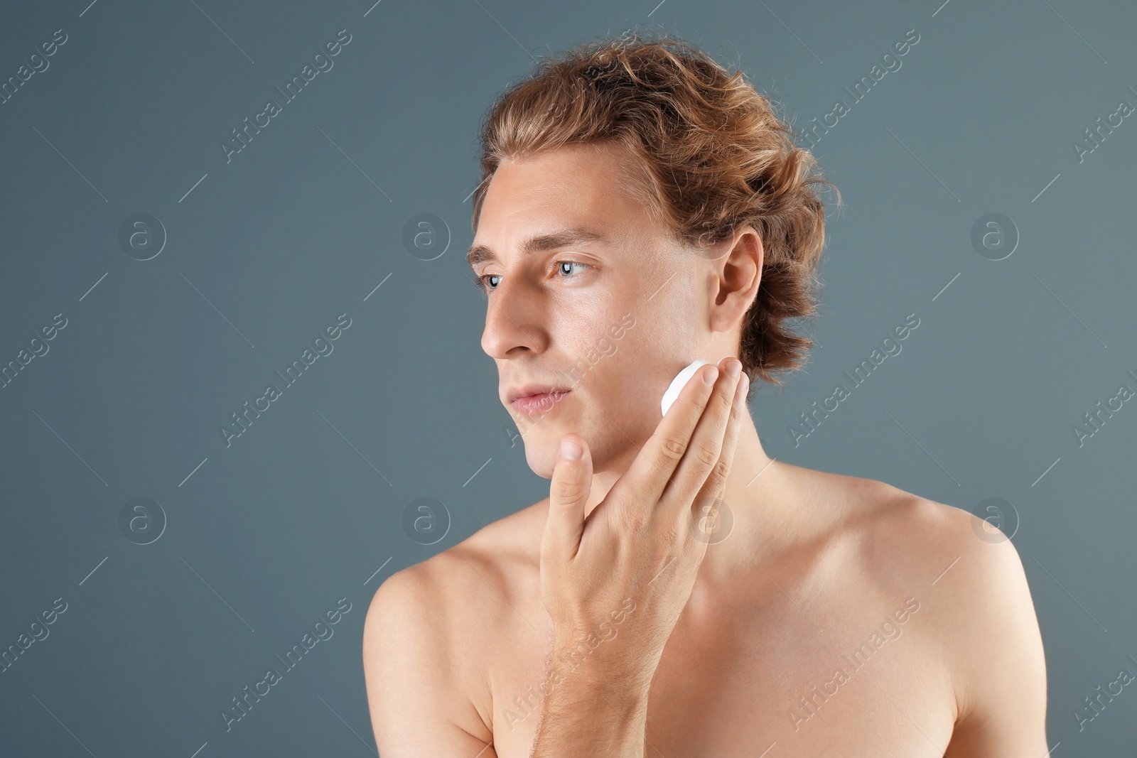 Photo of Young man applying shaving foam on gray background