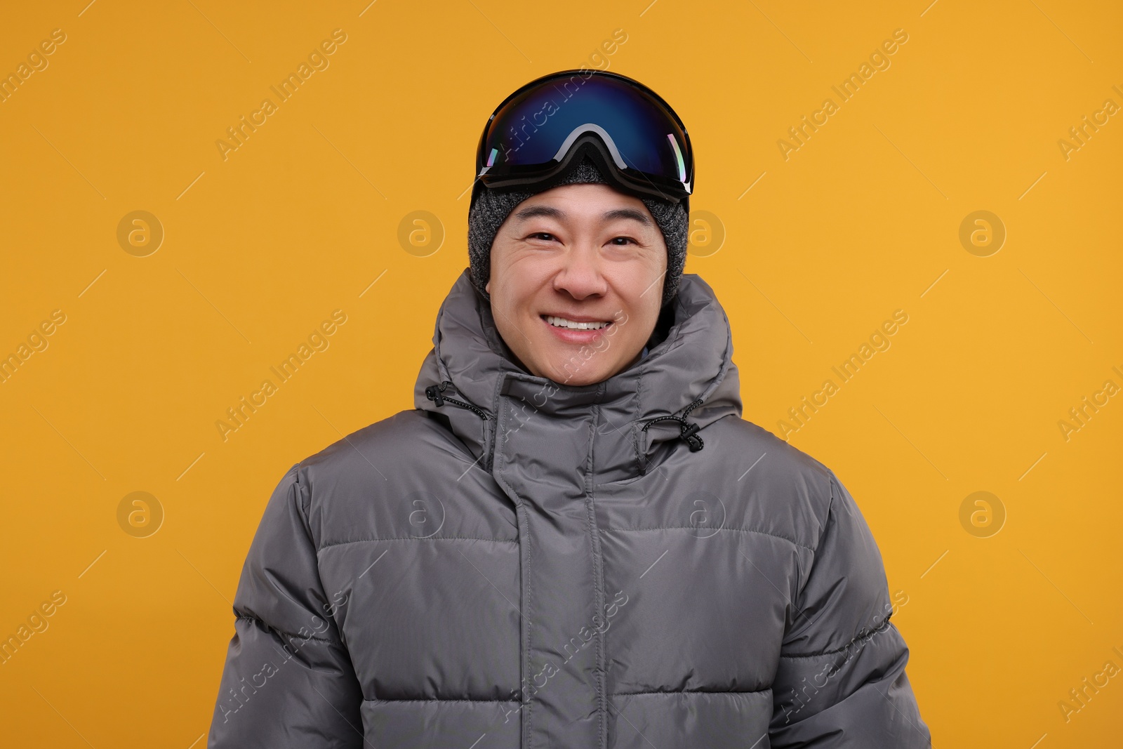 Photo of Winter sports. Happy man with ski goggles on orange background