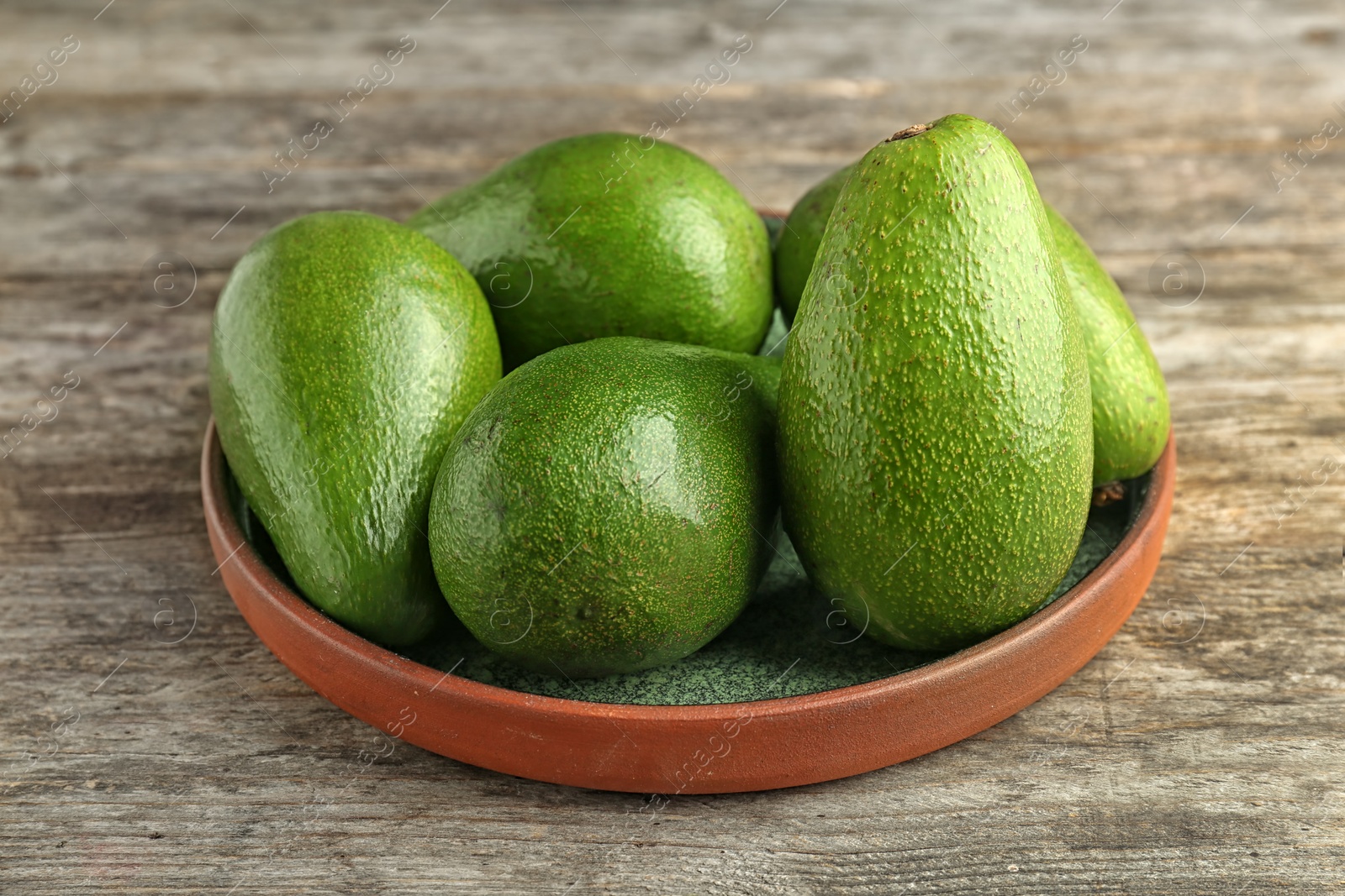 Photo of Plate with ripe avocados on wooden background