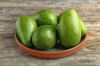 Plate with ripe avocados on wooden background