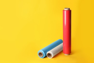 Photo of Different plastic stretch wrap films on yellow background, space for text