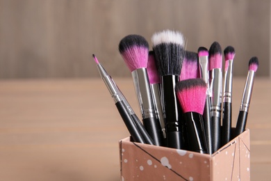 Photo of Organizer with makeup brushes on wooden table. Space for text