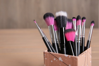 Organizer with makeup brushes on wooden table. Space for text