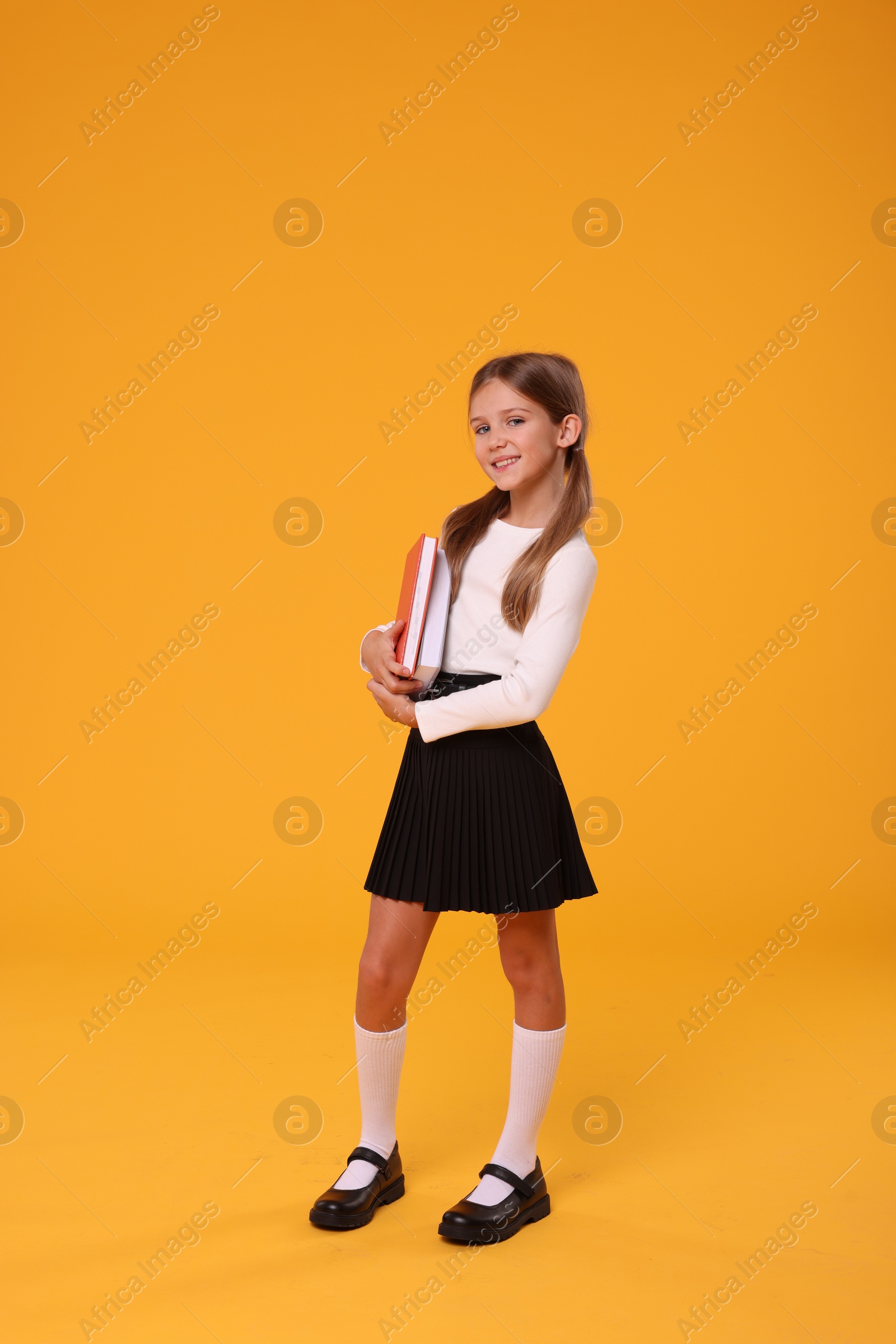 Photo of Happy schoolgirl with books on orange background