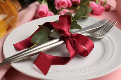 Photo of Romantic place setting. Plate, cutlery, eucalyptus branch and roses on table, closeup