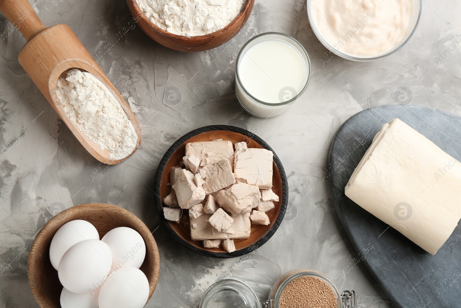 Photo of Pieces of compressed yeast and ingredients for dough on grey table, flat lay