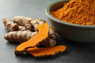 Photo of Bowl with turmeric powder and raw roots on grey table, closeup
