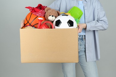 Photo of Woman holding box of unwanted stuff on grey background, closeup