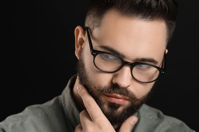 Young man with mustache touching face on black background