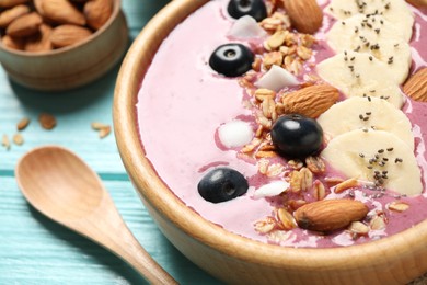 Photo of Delicious acai smoothie with granola and almonds in dessert bowl on light blue wooden table, closeup