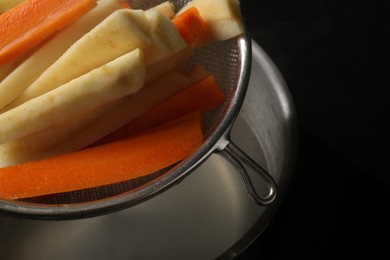 Sieve with cut parsnips and carrots over pot of water, closeup