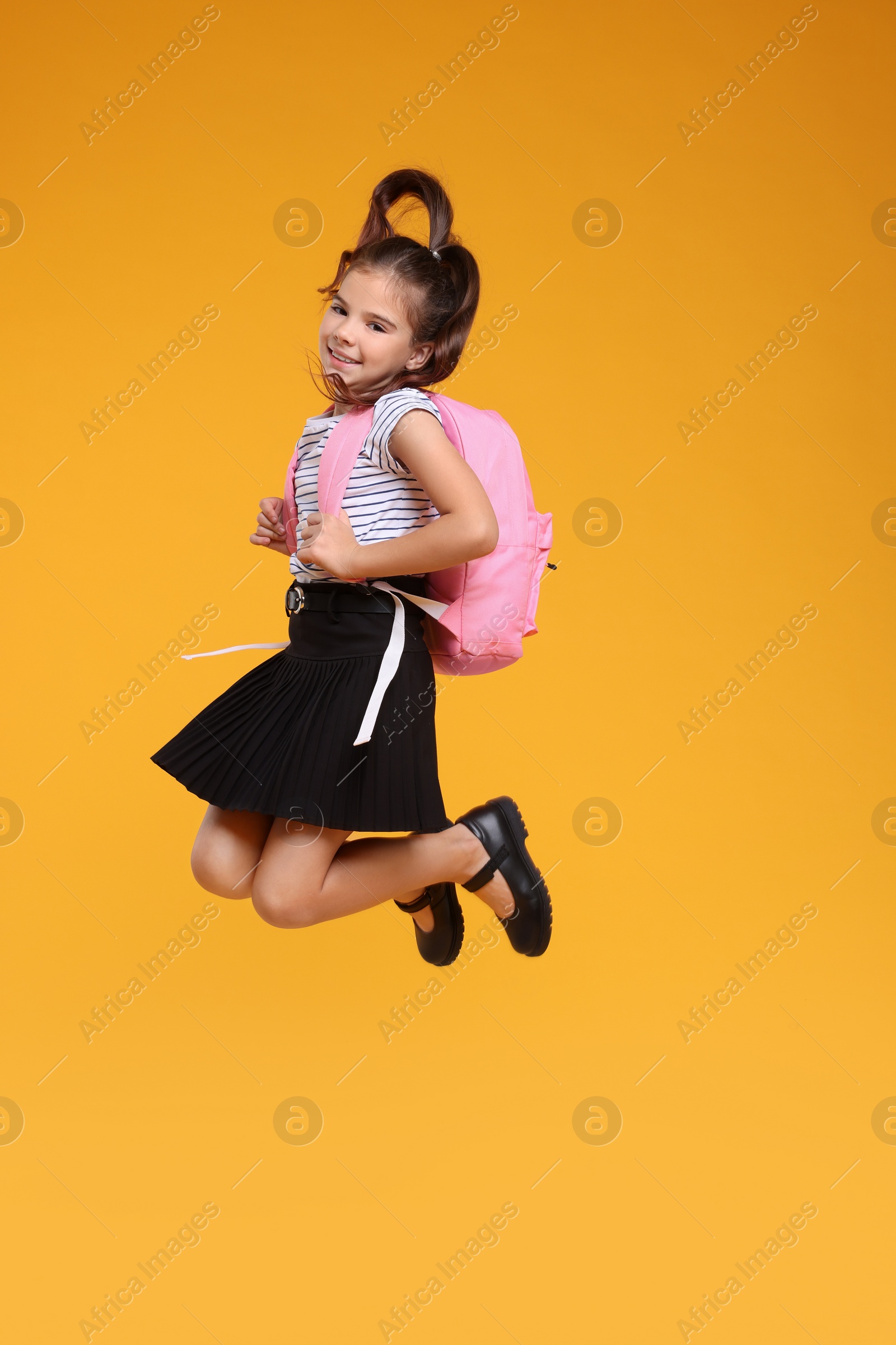 Photo of Cute schoolgirl jumping on orange background, space for text