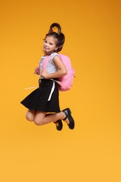 Photo of Cute schoolgirl jumping on orange background, space for text