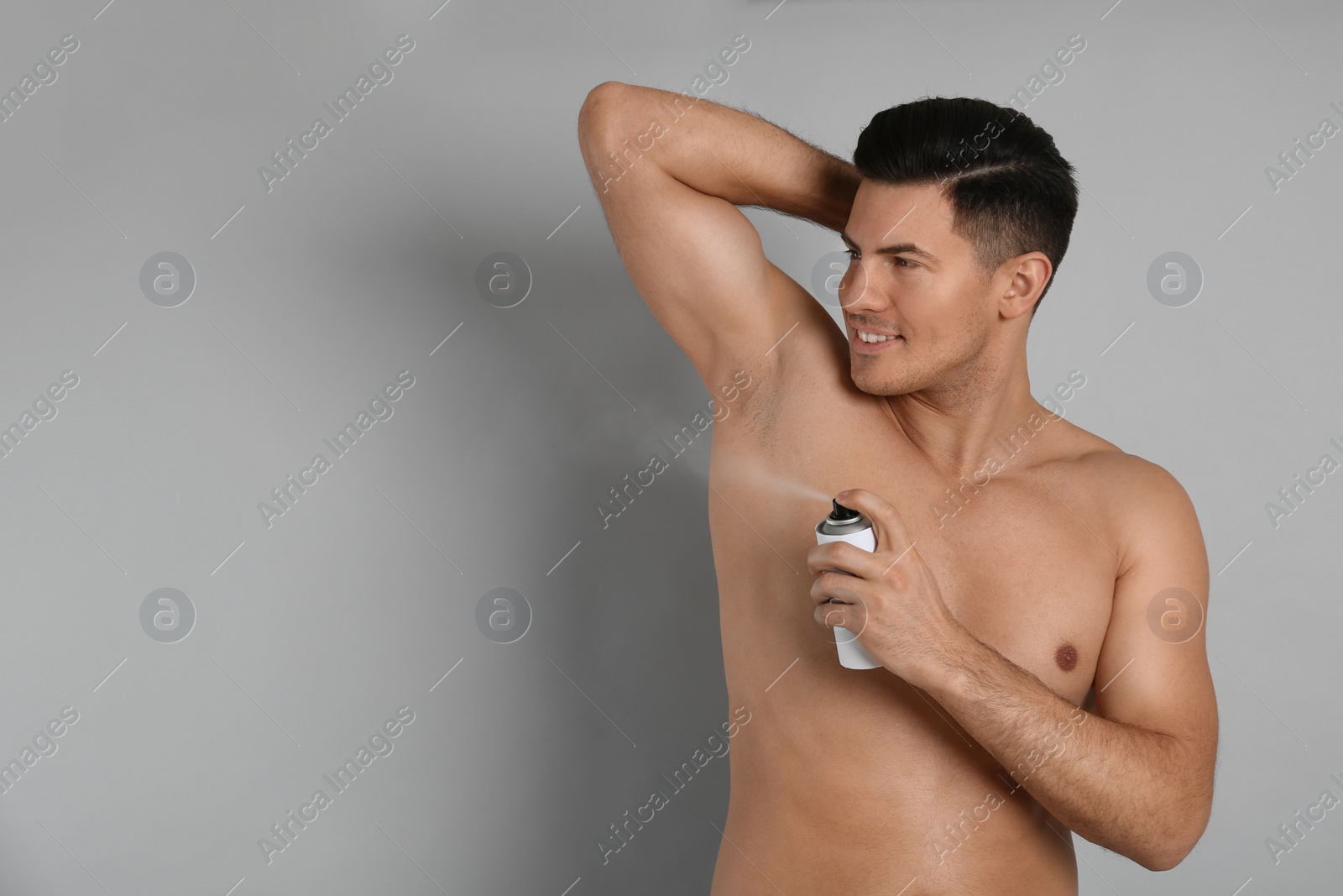 Photo of Handsome man applying deodorant to armpit on grey background, space for text