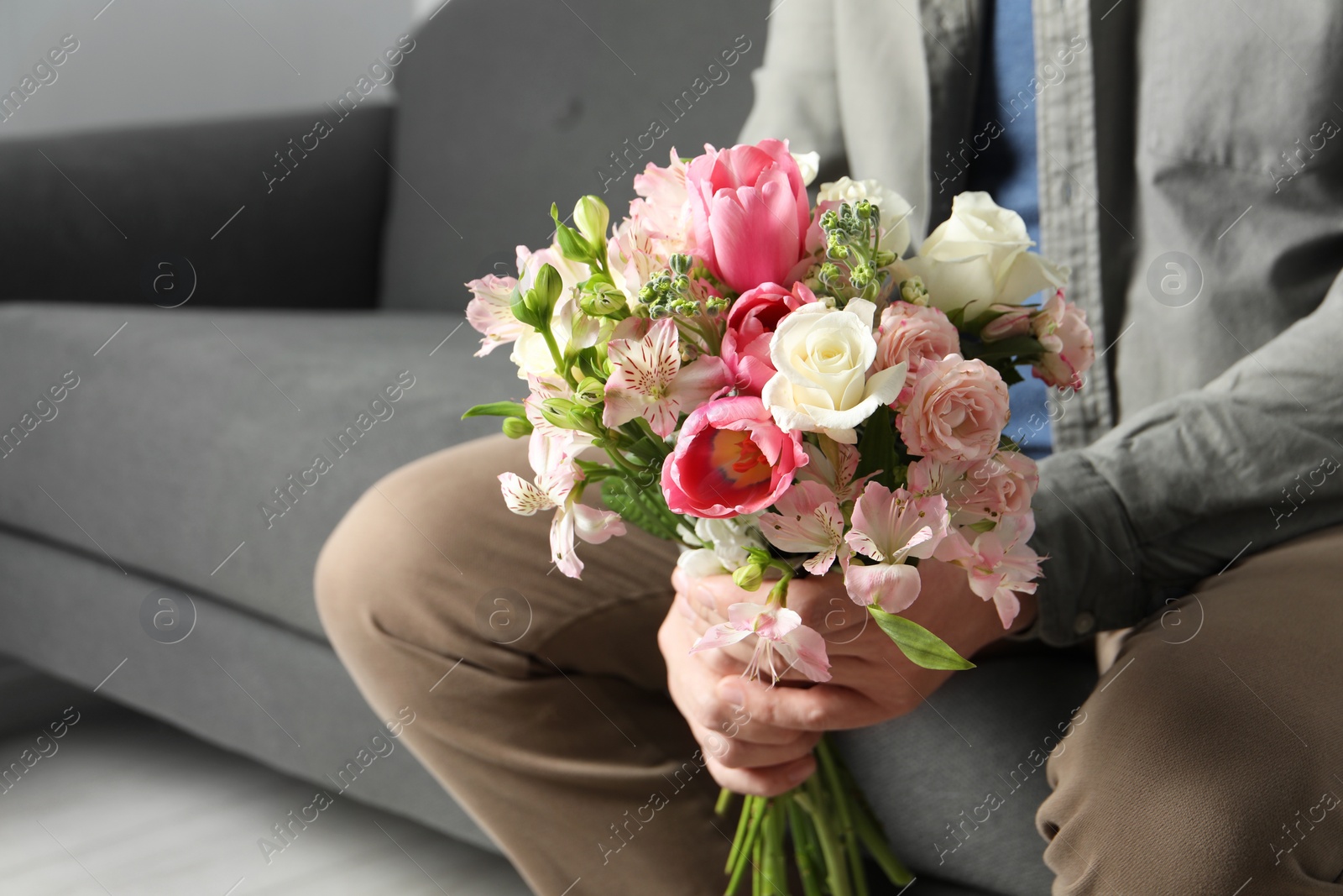 Photo of Man holding bouquet of beautiful flowers indoors, closeup