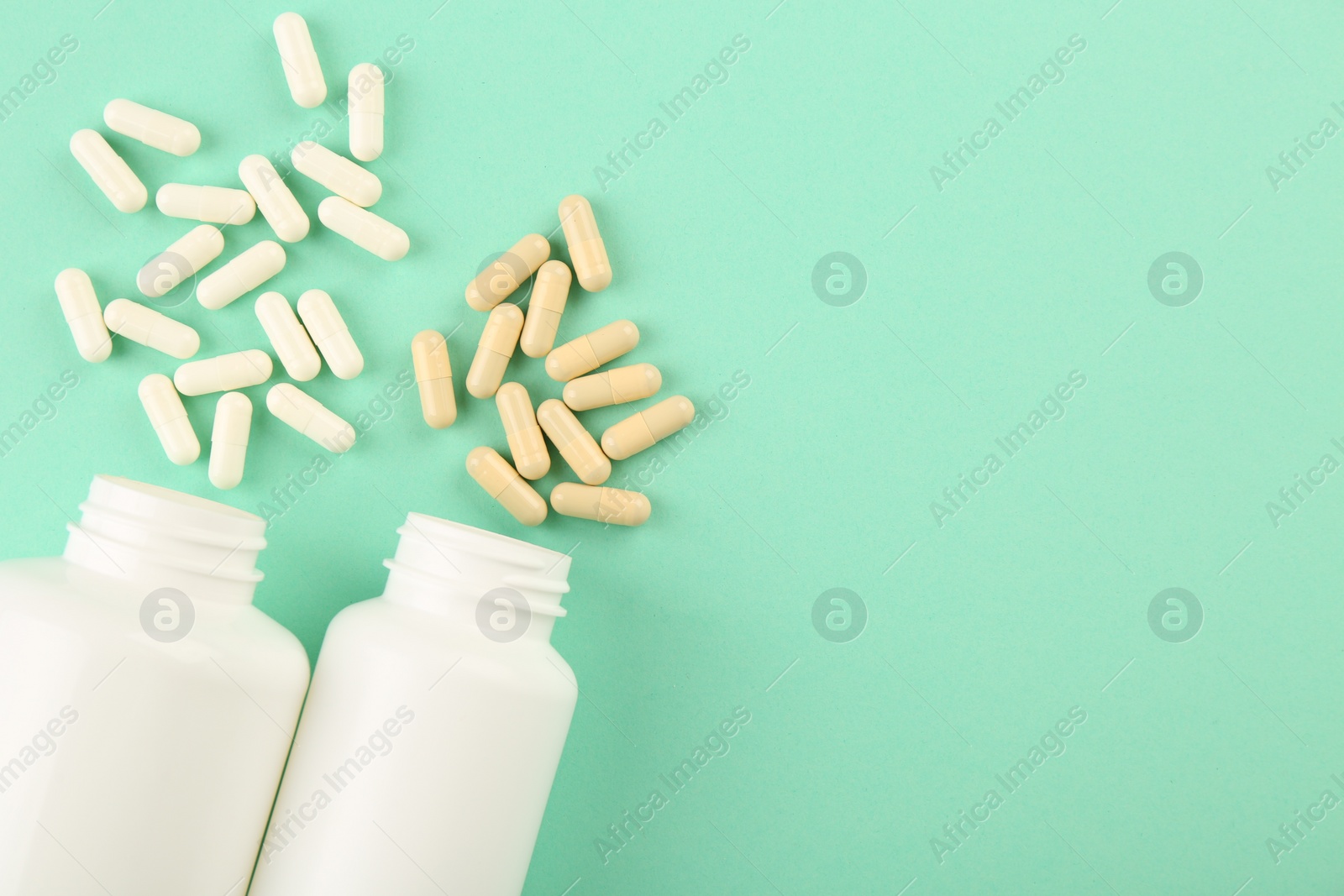 Photo of Bottles and different vitamin capsules on turquoise background, flat lay. Space for text