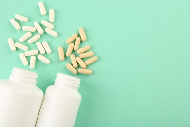 Photo of Bottles and different vitamin capsules on turquoise background, flat lay. Space for text