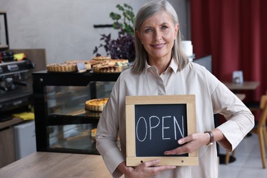 Happy business owner holding open sign in her cafe, space for text