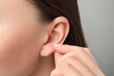 Woman touching her ear on light grey background, closeup
