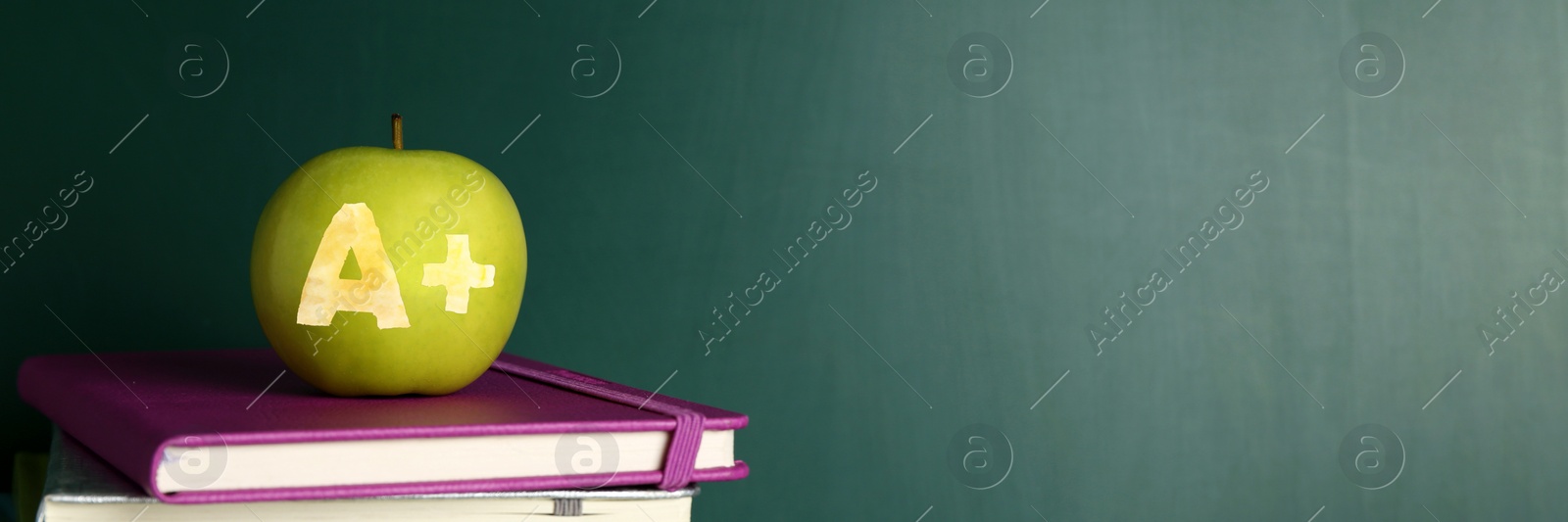 Image of Apple with carved letter A and plus symbol as school grade on books near green chalkboard. Banner design with space for text