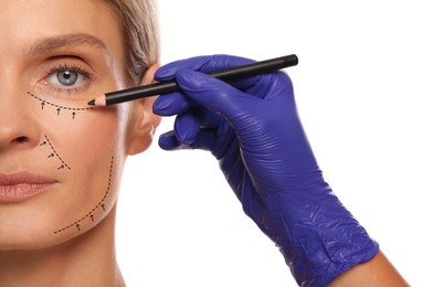 Woman preparing for cosmetic surgery, white background. Doctor drawing markings on her face, closeup