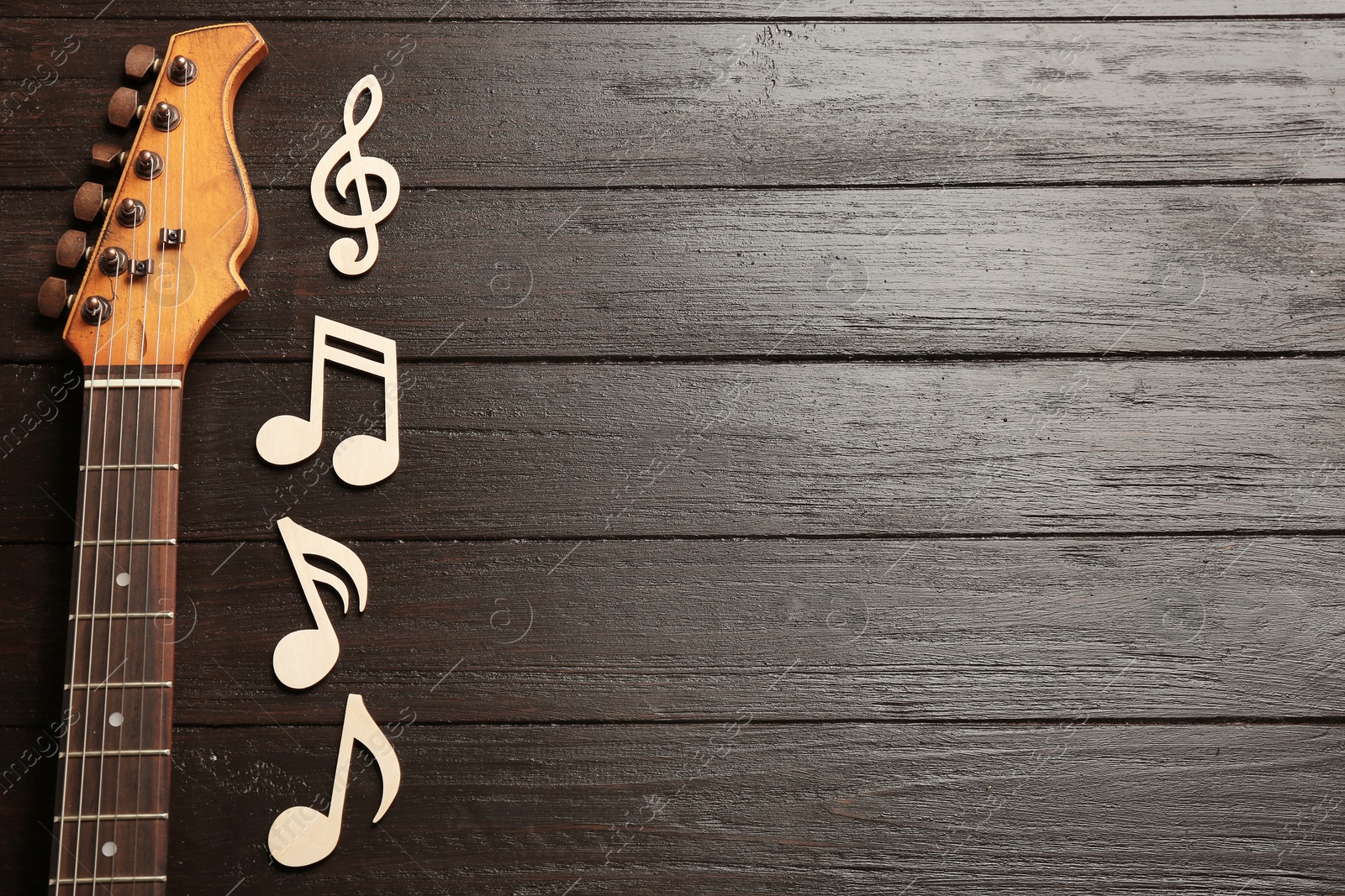 Photo of Music notes and guitar neck on wooden background, top view. Space for text