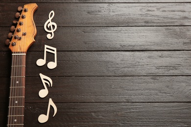 Photo of Music notes and guitar neck on wooden background, top view. Space for text