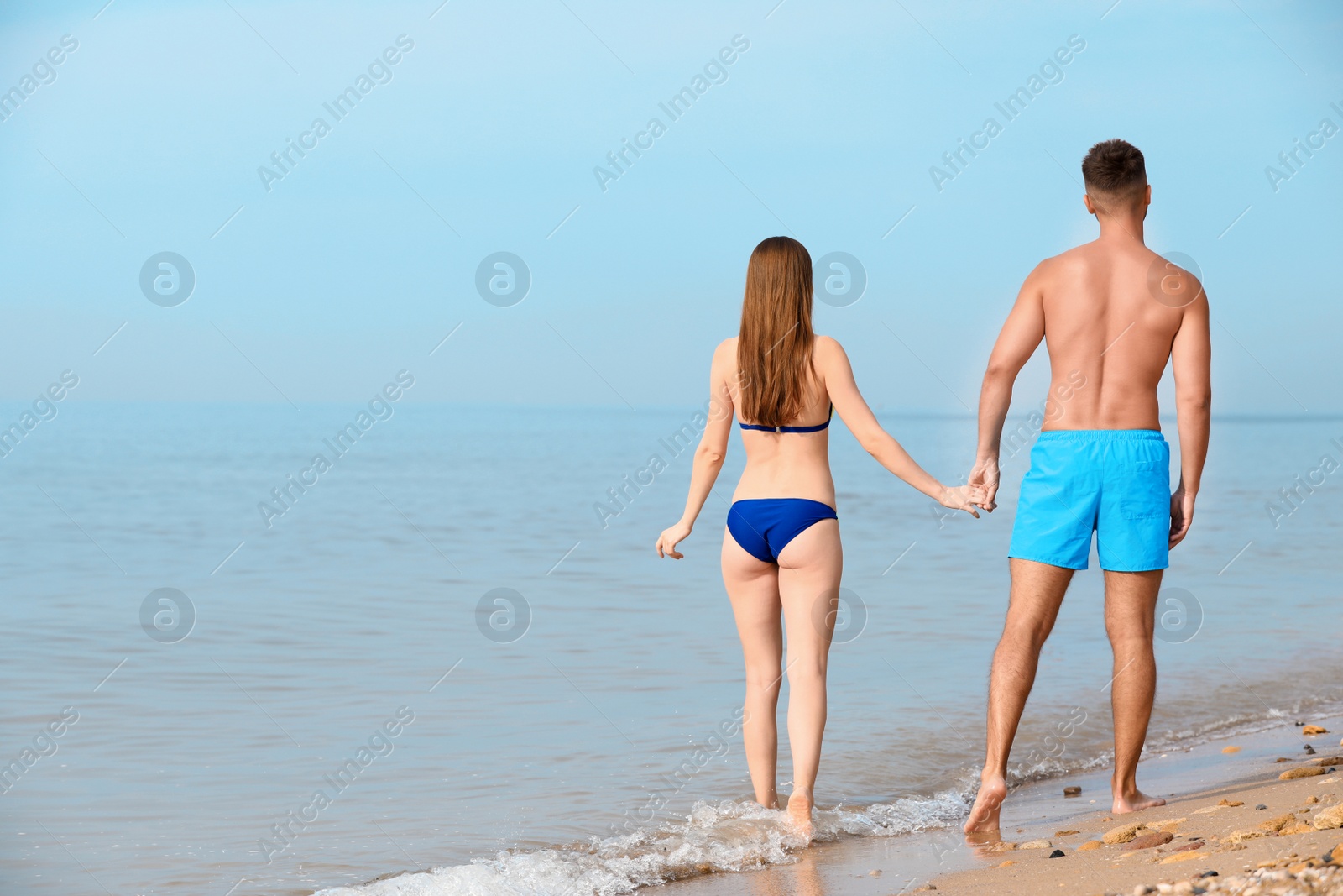 Photo of Young woman in bikini with her boyfriend walking on beach, space for text. Lovely couple