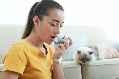 Photo of Young woman using asthma inhaler near cat at home. Health care