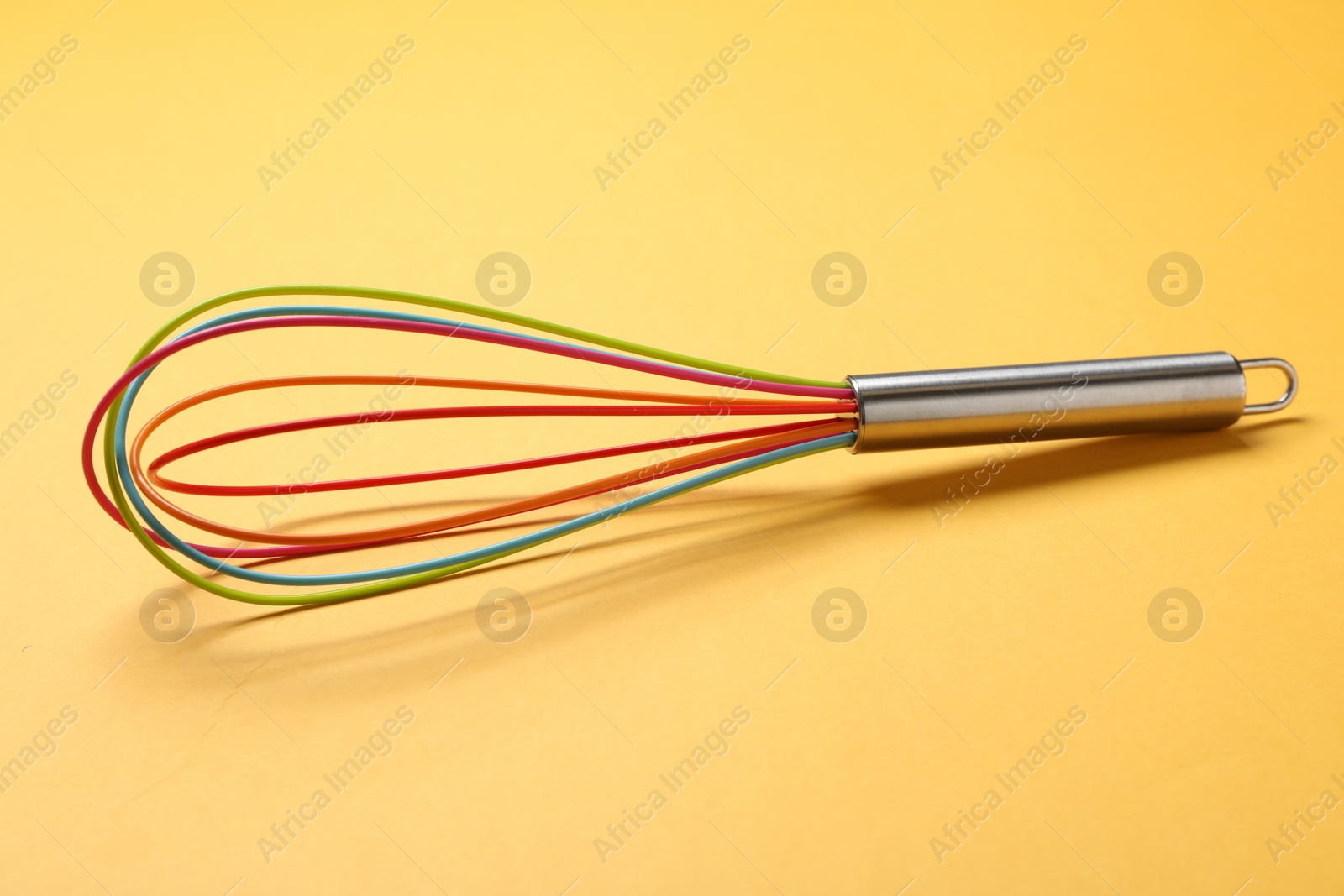 Photo of Bright whisk on yellow background. Kitchen tool