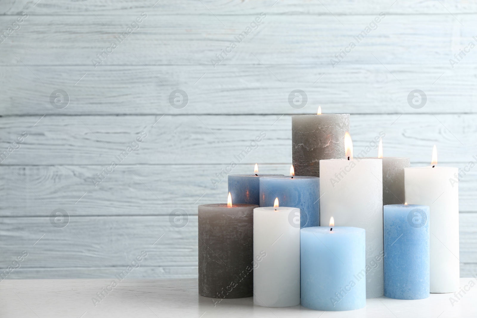 Photo of Set of burning candles on table against light wooden background. Space for text