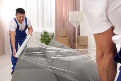 Workers wrapping sofa in stretch film indoors