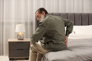 Senior man suffering from back pain on bed at home. Rheumatism symptom